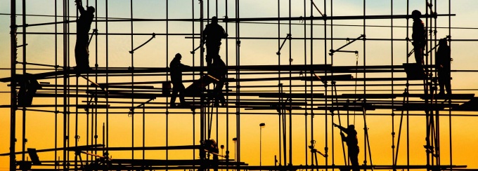 Silhoutettes of workers working on a scaffolding. 