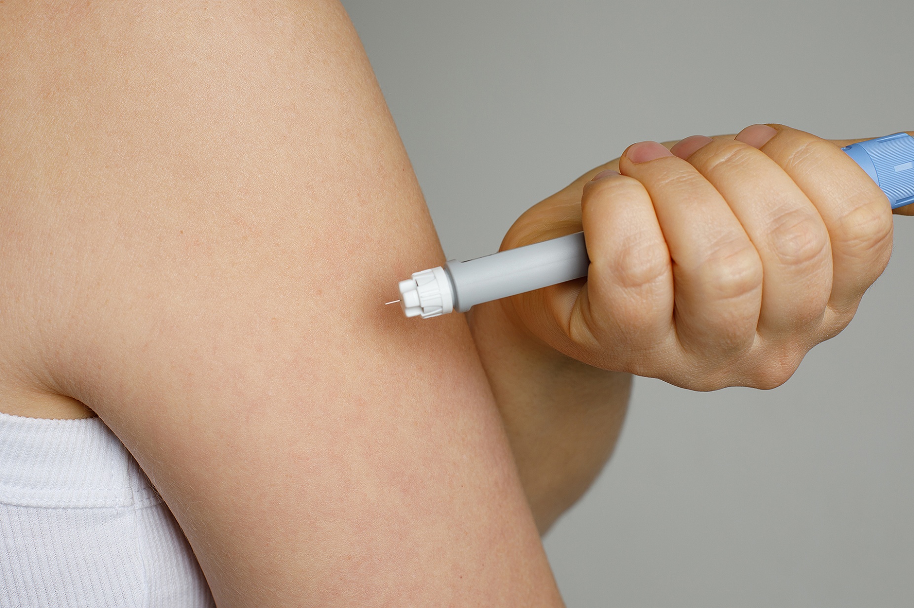 Close view of a person using a weight-loss medication injection pen in their upper arm. 