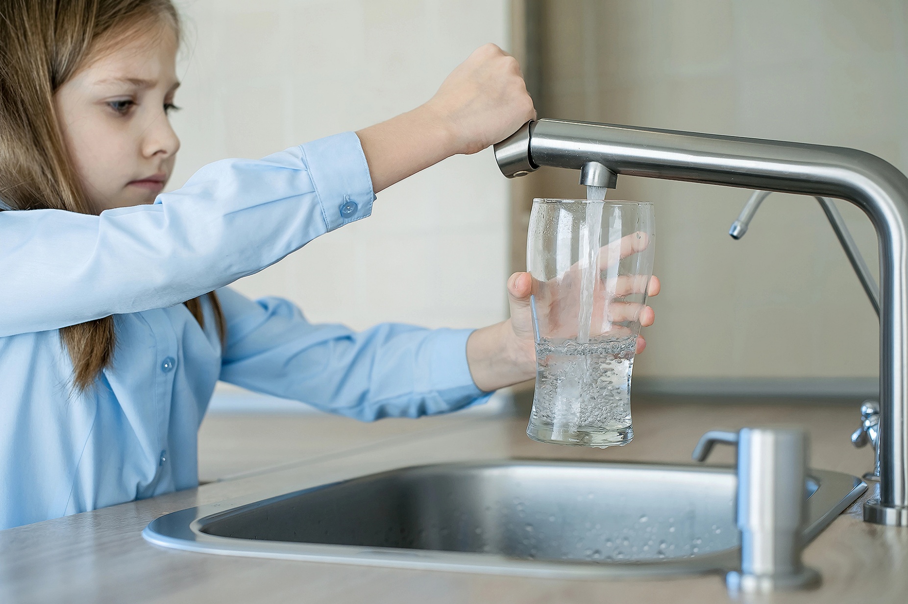A child gets a glass of water from a kitchen tap. 