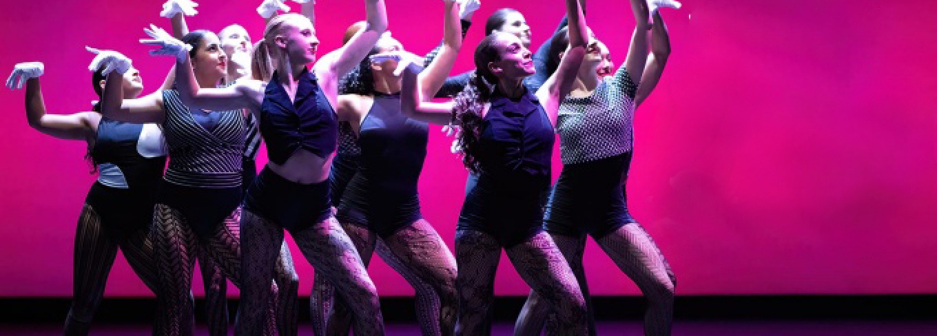 A group of dancers together in front of a hot pink background.