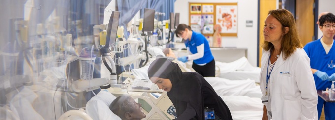 Image shows nursing students working in a simulated hospital as instrcutors look on. 