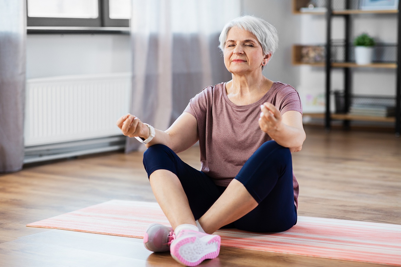 A senior woman practices mindfulness while sitting on a yoga mat. 