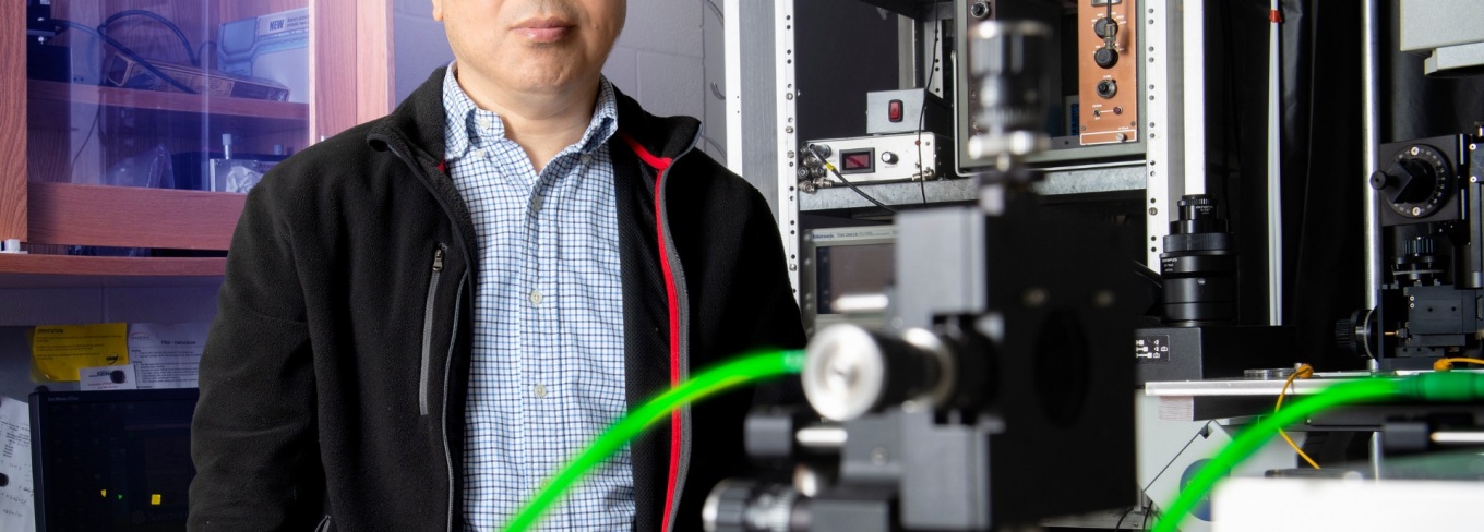 Feng Qin is standing behind equipment in his lab. 