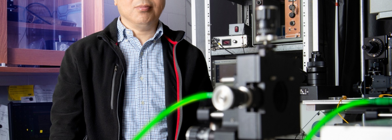 Feng Qin is standing behind equipment in his lab.