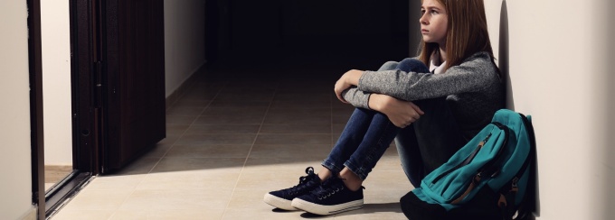 A student sitting alone in a hall with her bookbag. 