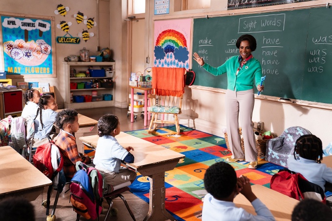 A scene from Abbott Elementary "No Homework" episode featuring a classroom of young studenbts and a smiling teacher in front of a blackboard.