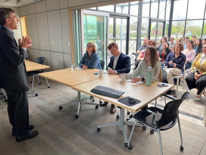 Zoom image: Guest judges Mary Odden, Ethan Smith, and Sadie Kratt, all alums of the CRC class (2024, 2021, and 2019, respectively) watch as Ryan McPherson introduces the final presentations of the Carbon Reduction Challenge, with clients and students present in the UB GRoW Home. 