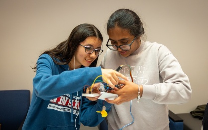 Two teenagers smile while working together on a STEM project. 