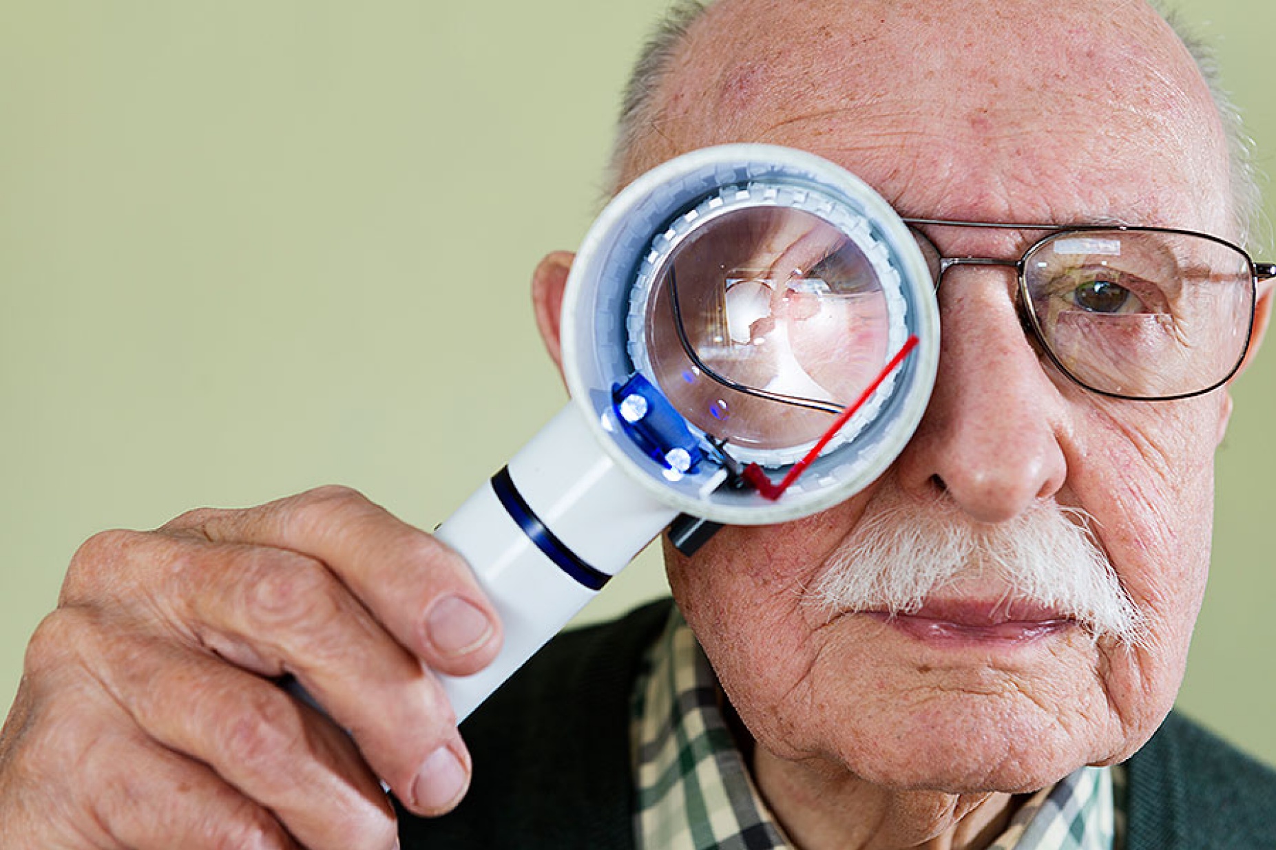 Elderly man peers through a magnifying glass. 
