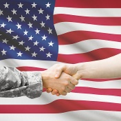 soldier and civilian hold hands in front of US flag. 