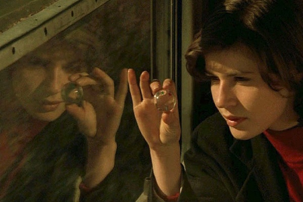 Scene from Double Life of Veronique. The star, Irene Jacob stares through a small glass orb and her image is reflected in a window. 