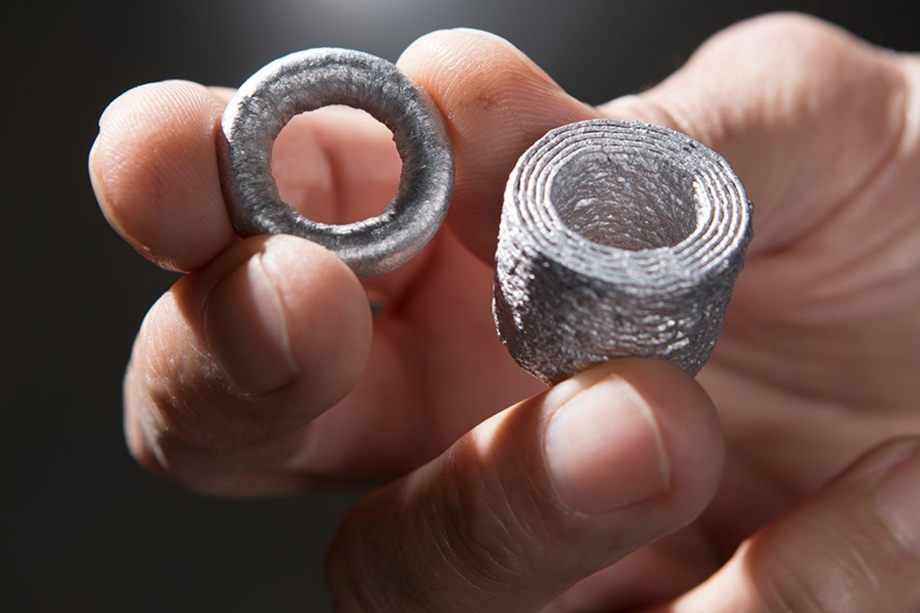Close-up of a hand holding aluminum pieces printed using a Vader machine. 
