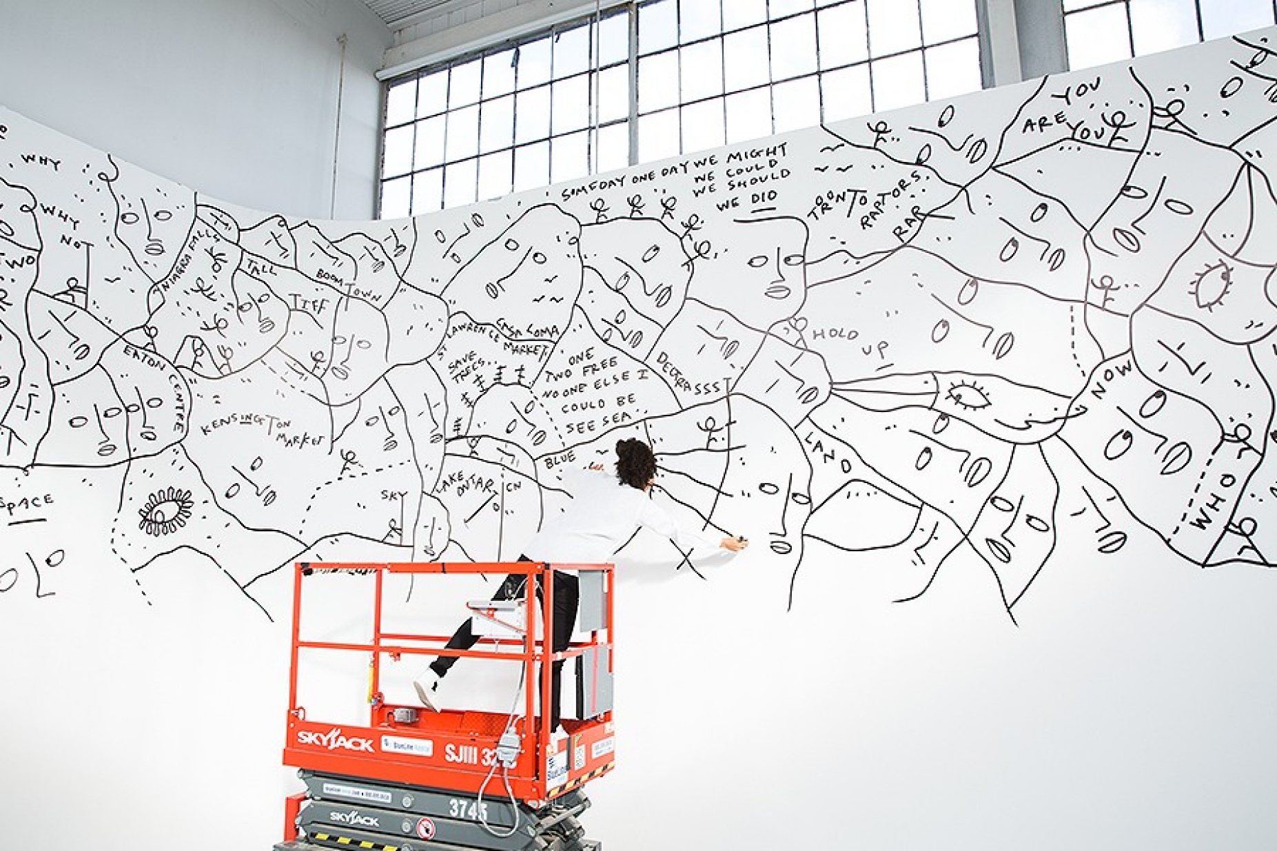 Shantell Martin, on a scissor-lift, creating a mural. 