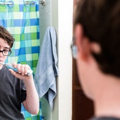 Bored looking teenage boy, brushing his teeth in front of a mirror. 