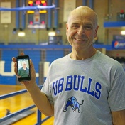 Michael May on track in Alumni Arena with a smartphone showing a photo of his 80-pound heavier self. 