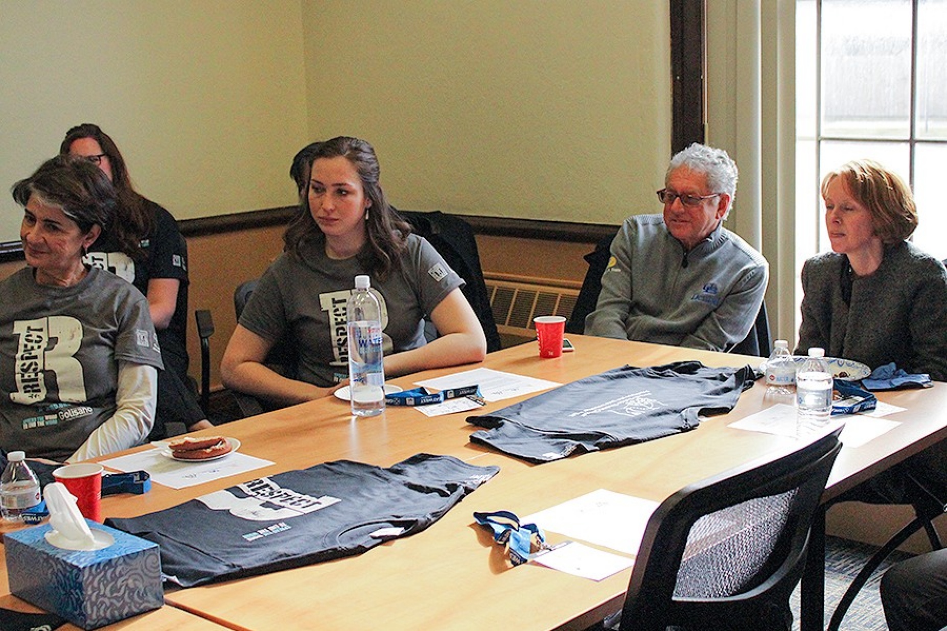 Smile day volunteers, including Ann Costello and Steven Perlman, sit around a table and listen to a welcome from M. Dian ChinKit-Wells, who is off camera.