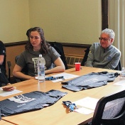 Smile day volunteers, including Ann Costello and Steven Perlman, sit around a table and listen to a welcome from M. Dian ChinKit-Wells, who is off camera. 
