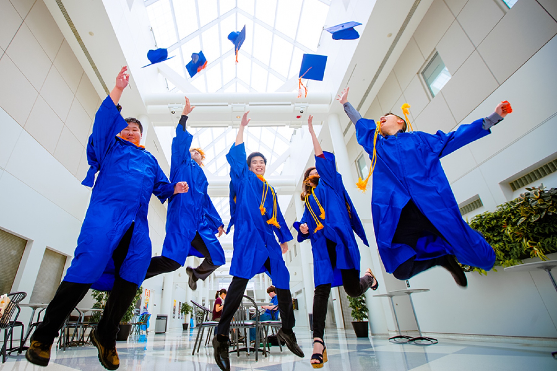 Graduates jump and throw their caps in the air in the CFA atrium. 