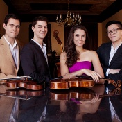 members of the Dover String Quartet leaning on a piano. 