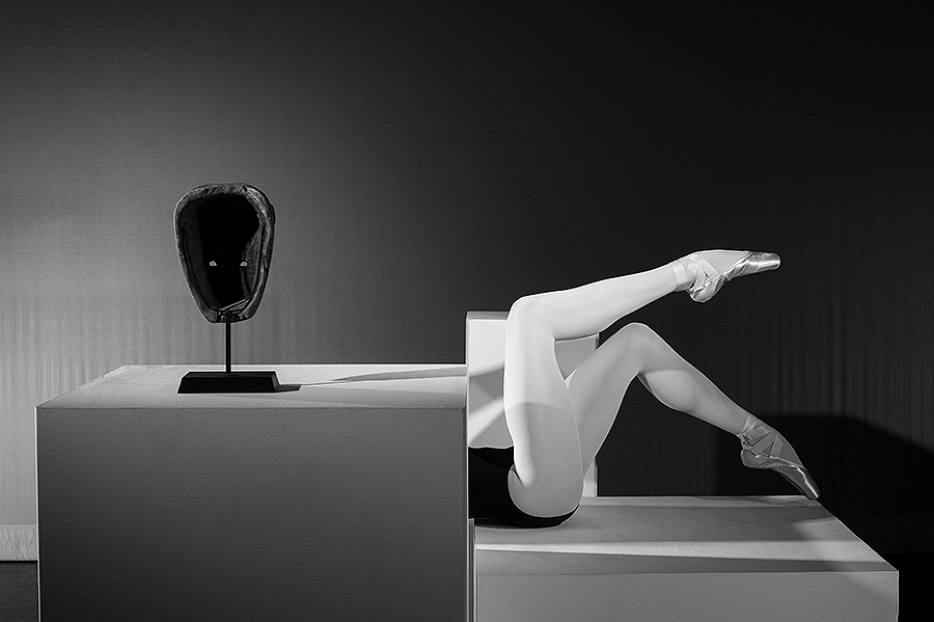 Brendan Fernandes. As One IX, 2017. Photograph on paper. Courtesy of the artist. African mask sitting near mannequin legs in ballet slippers. 