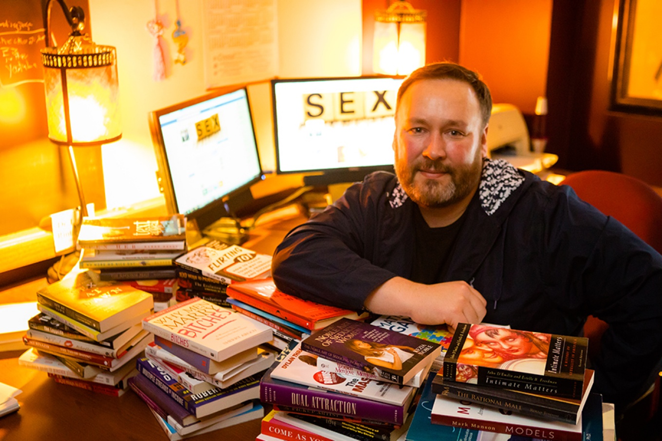 Lance Rintamaki in his office, books strewn across his desk, the word SEX visible on a computer behind him.