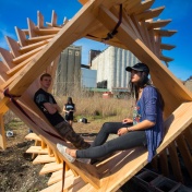 Two students sit in one of the wooden Reflection Space structures. 