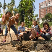 Photograph of young girls participating in the "Endless Orchard" project, digging a hole to plant fruit trees. 