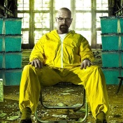 Walter White character from Breaking Bad wearing a yellow hazmat suit, sitting in a lawn chair in a warehouse surrounded by stacks of money and bins filled with "Blue Sky" meth. 