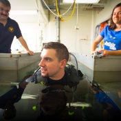 Dave Hostler looking on while a diver wearing a wetsuit crouches in a small pool. 