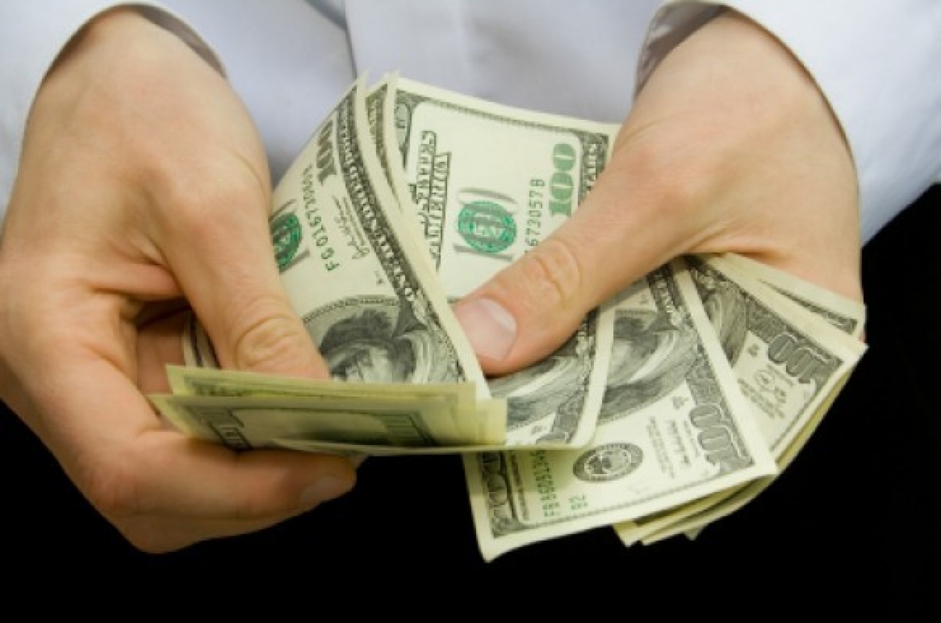 photo shows a man's hands handling a stack of $100 bills. 
