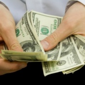 photo of a man's arms and hands handling a stack of $100 bills. 