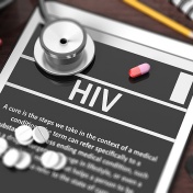 Tablet with "HIV" on screen, stethoscope, pills and objects on wooden desktop. 