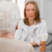Elderly woman seen from the rear, with a doctor in the background. 