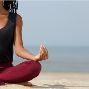 African woman practicing yoga on a beach. 