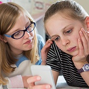 girl on her phone being cyberbullied; caring friend looks on. 
