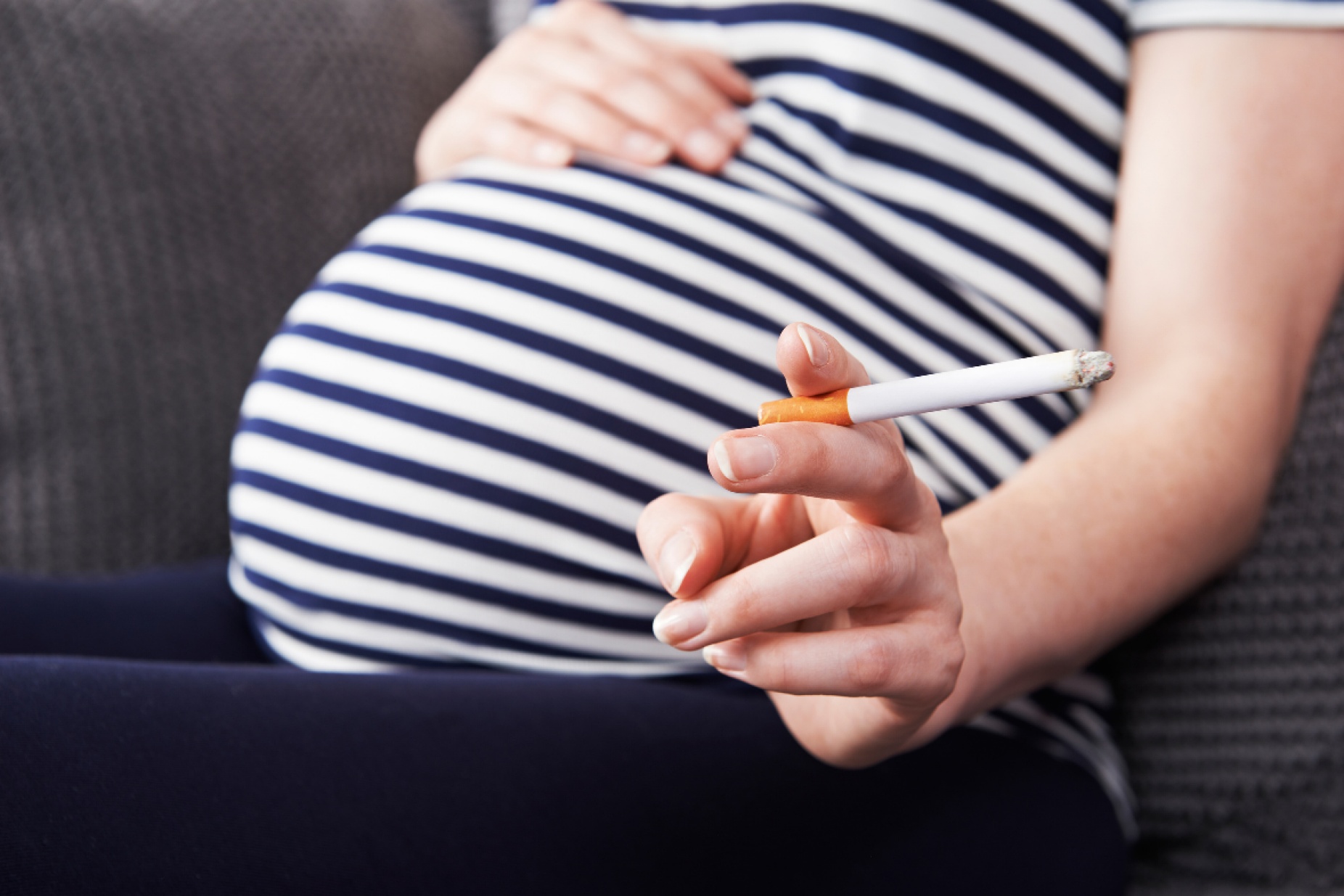 Pregnant woman from the neck down, she's hold a light cigarette. 