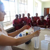 A GEC volunteer does an experiment with Kitenga students to clean dirty water. 