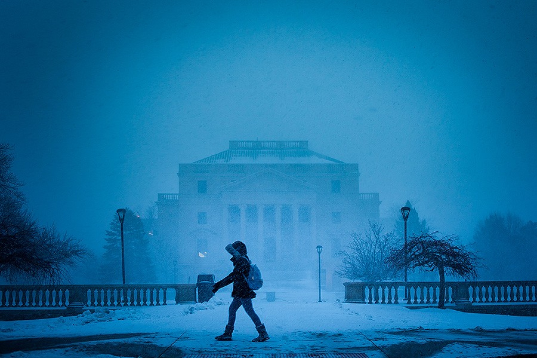 Student bundled in parka walking in from of the health sciences library in a snowstorm.