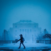 student bundled in parka walking in front of the Health Sciences Library in a snowstorm. 