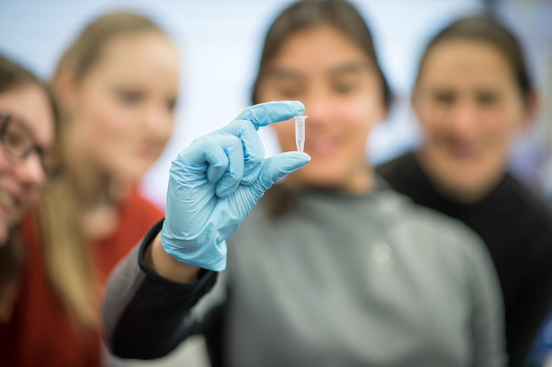 Young woman wearing latex glove holding a genetic sample vile. 