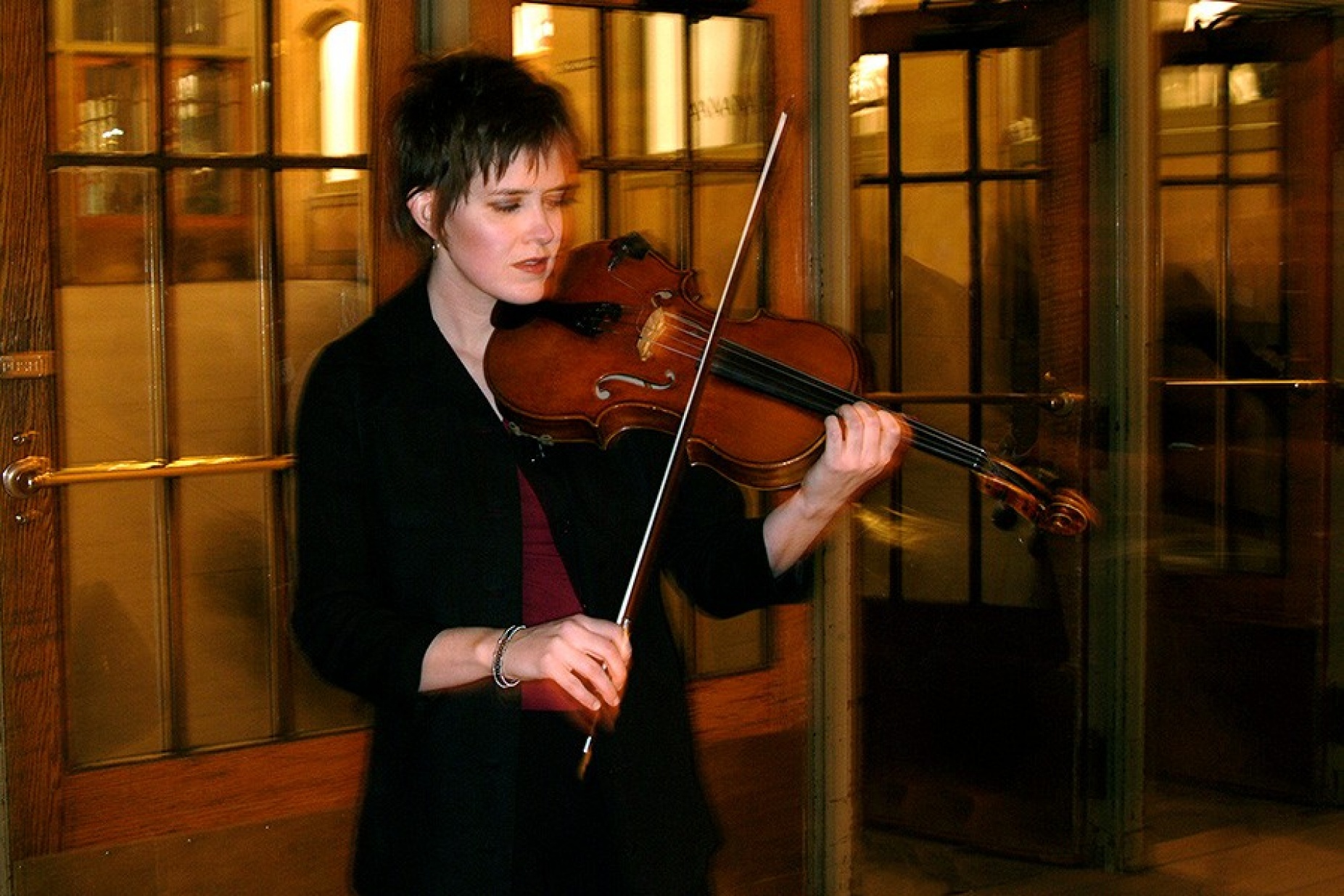 Leanne Darling playing her viola in front of a series of glass doors. 