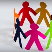 Inclusion concept: Multi-colored paper people cutouts in a circle ("holding hands") on a white background. 