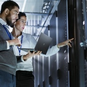 Man and women at mainframe computer; man also holds laptop. 
