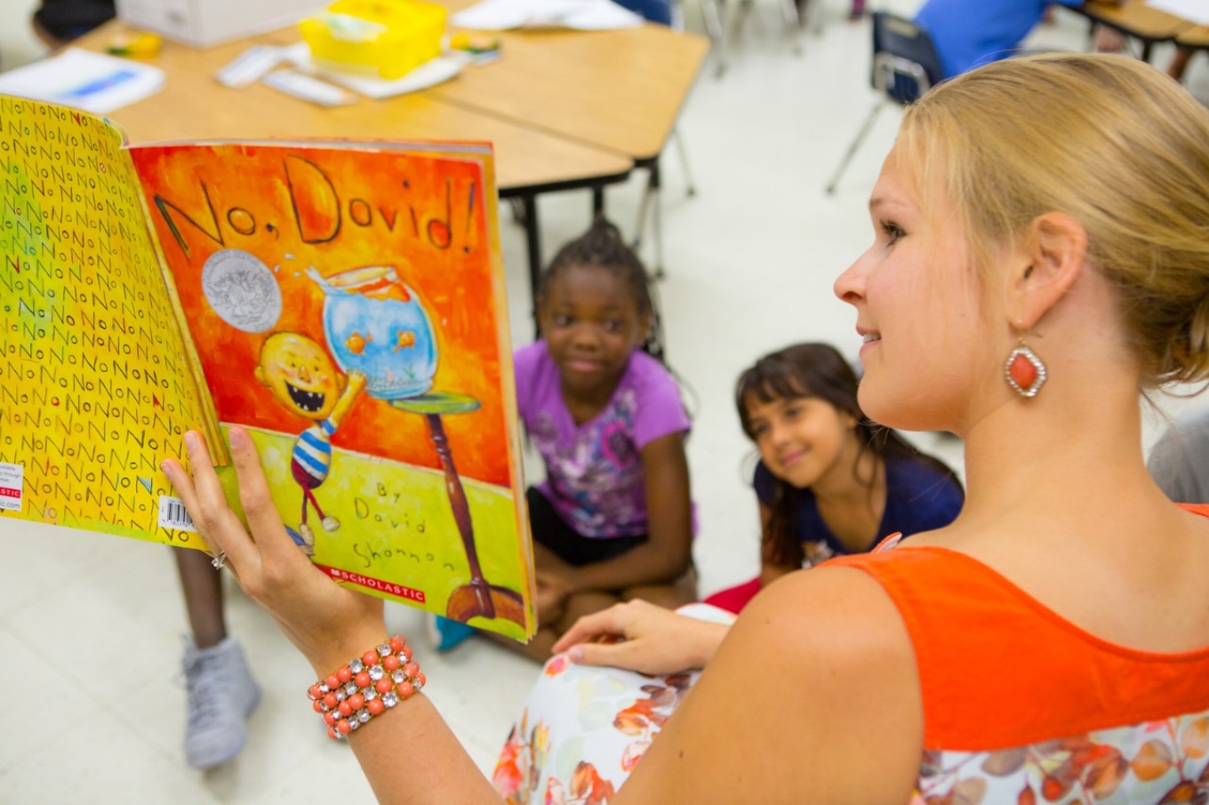 Photo of a woman teacher reading a book to two young girls in her class. 