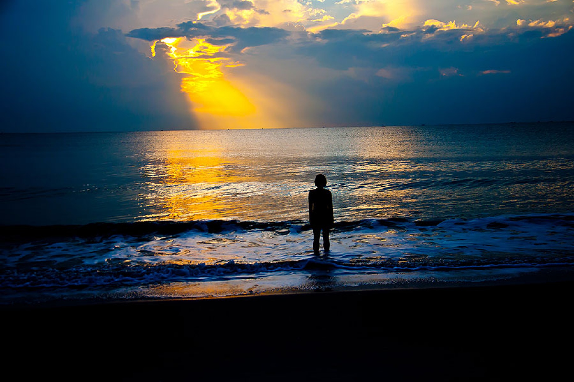 Silhouette of girl standing at the shore of the ocean watching the sun set. 