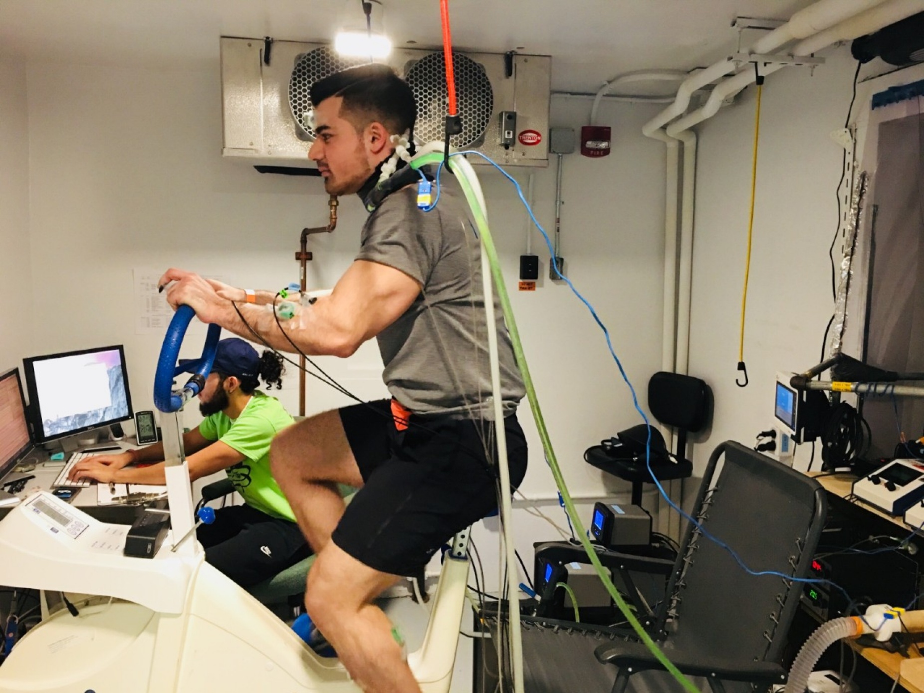 A male study participant on a stationery bike with a tubing unit on the back of his neck. 