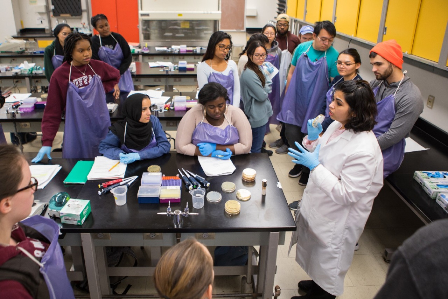 UB biological sciences lecturer Nitasha Sehgal (in white lab coat, holding petri dish) teaches in the CRISPR lab.