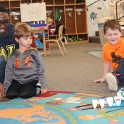 Teacher Stanley Diih, ECRC students Griffin Maines and Lochlan and the code-a-pillar on a world-map rug in an ECRC classroom. 