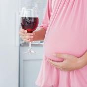 Pregnant woman, one hand on her belly the other holds a glass of wine. 