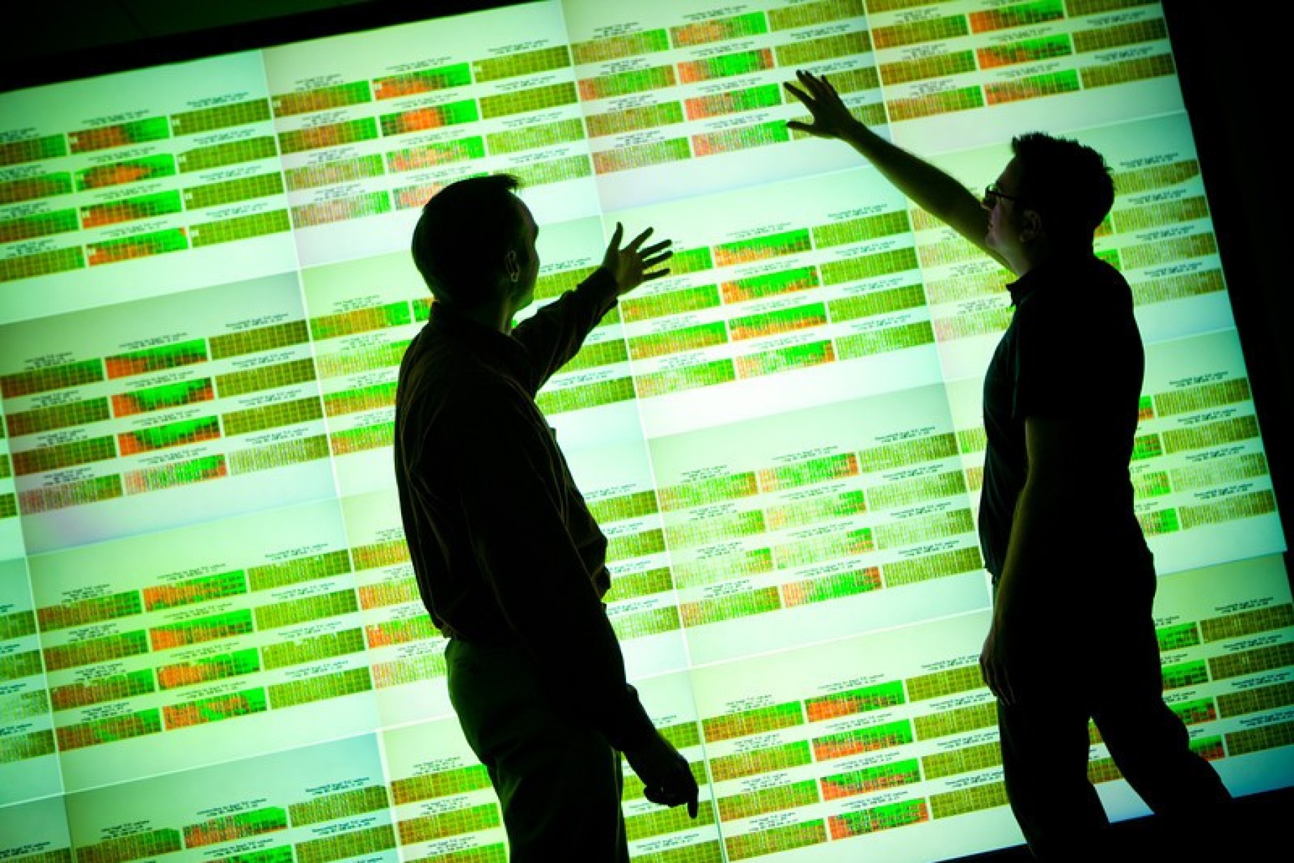 Silhouettes of men looking at an illuminated wall of big data.
